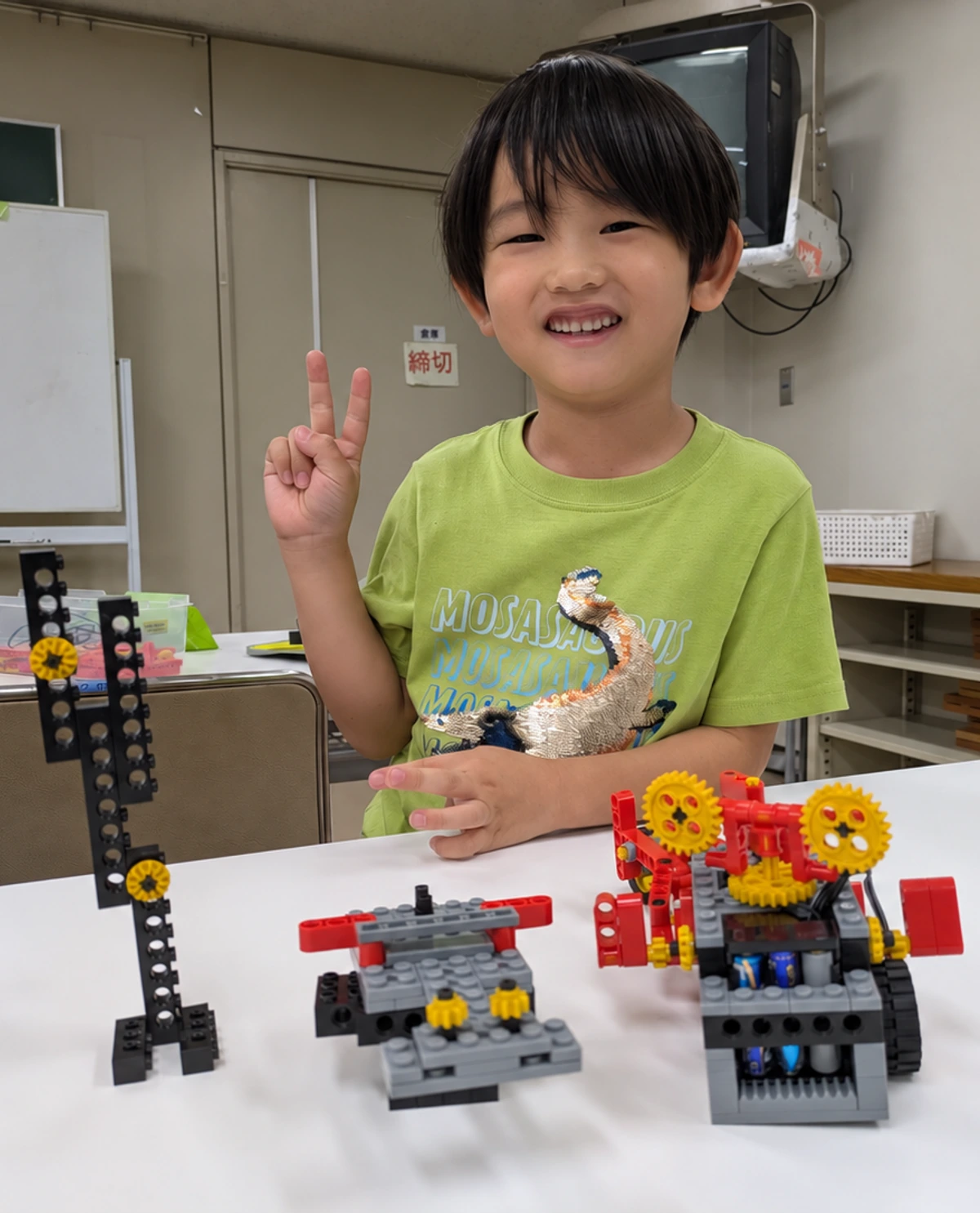 製作したロボットを机に並べ、笑顔でピースサインをするロボット教室の生徒